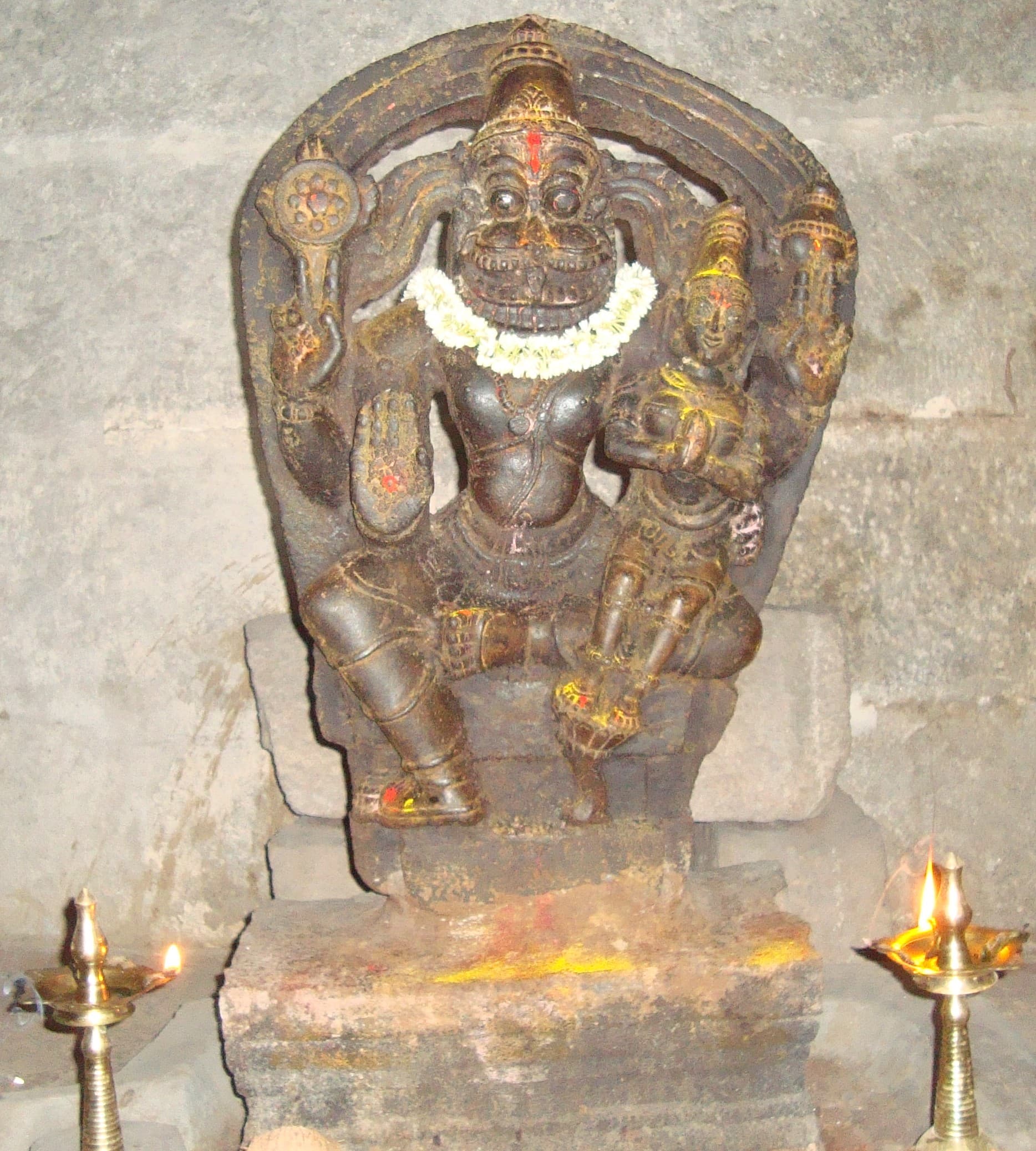 Stone relief of Lakshmi Narasimha at Gurramkonda, with flowers and two lit oil lamps.